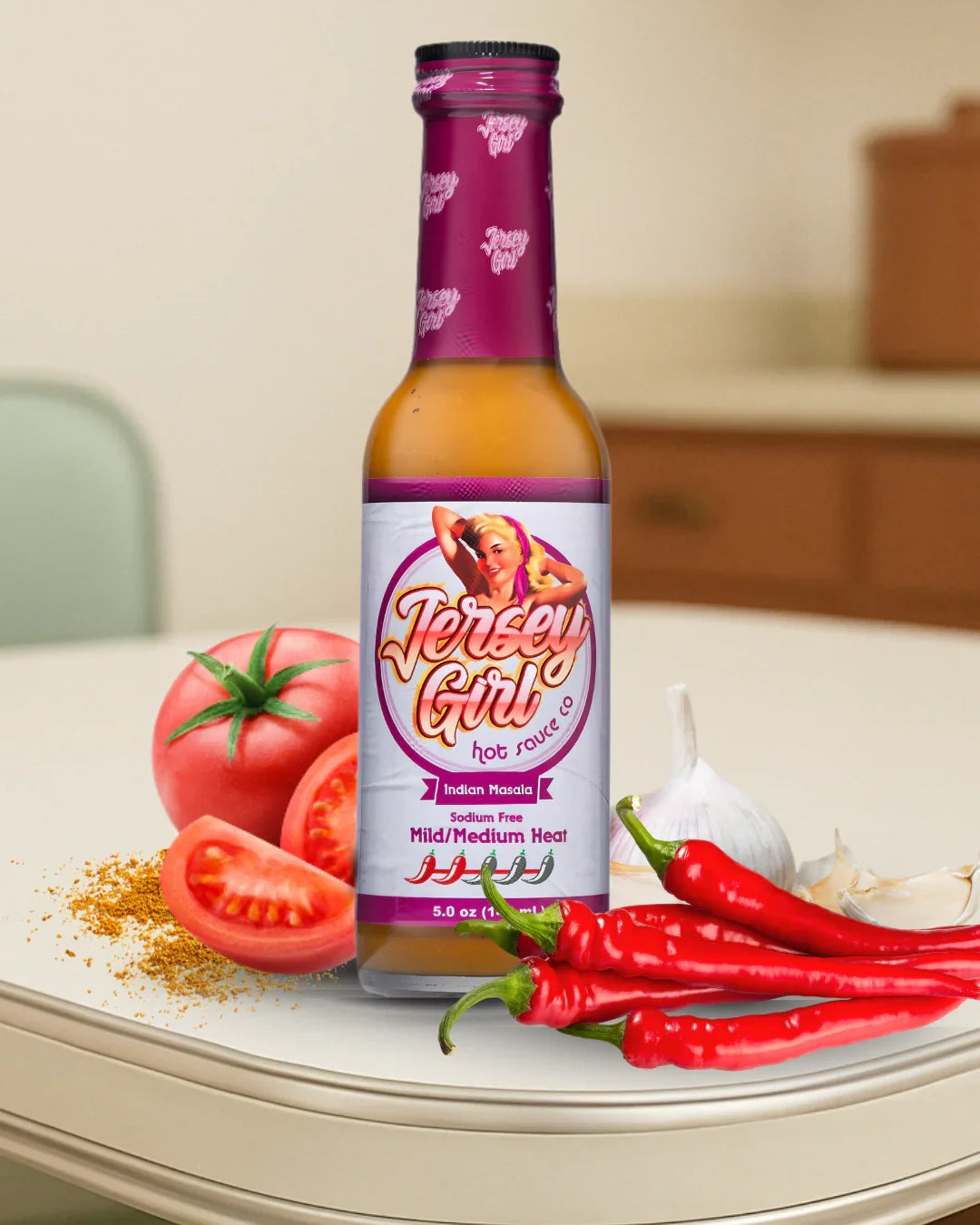 Jersey Girl Indian Masala Hot Sauce bottle on a kitchen counter, surrounded by fresh tomatoes, garlic, red chili peppers, and Indian spice blend. The label highlights it as a sodium-free hot sauce with mild to medium heat and bold Indian-inspired flavor.